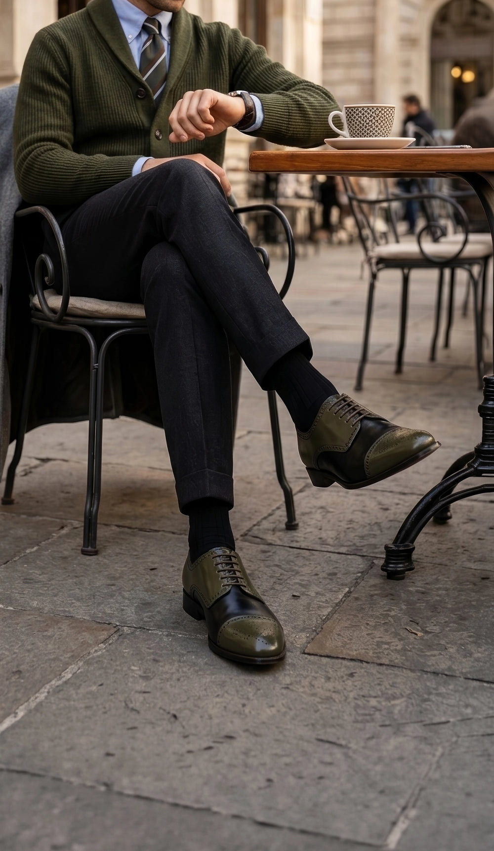 Man wearing Imperial Olive two-tone Oxford shoes with tailored trousers at an outdoor café
