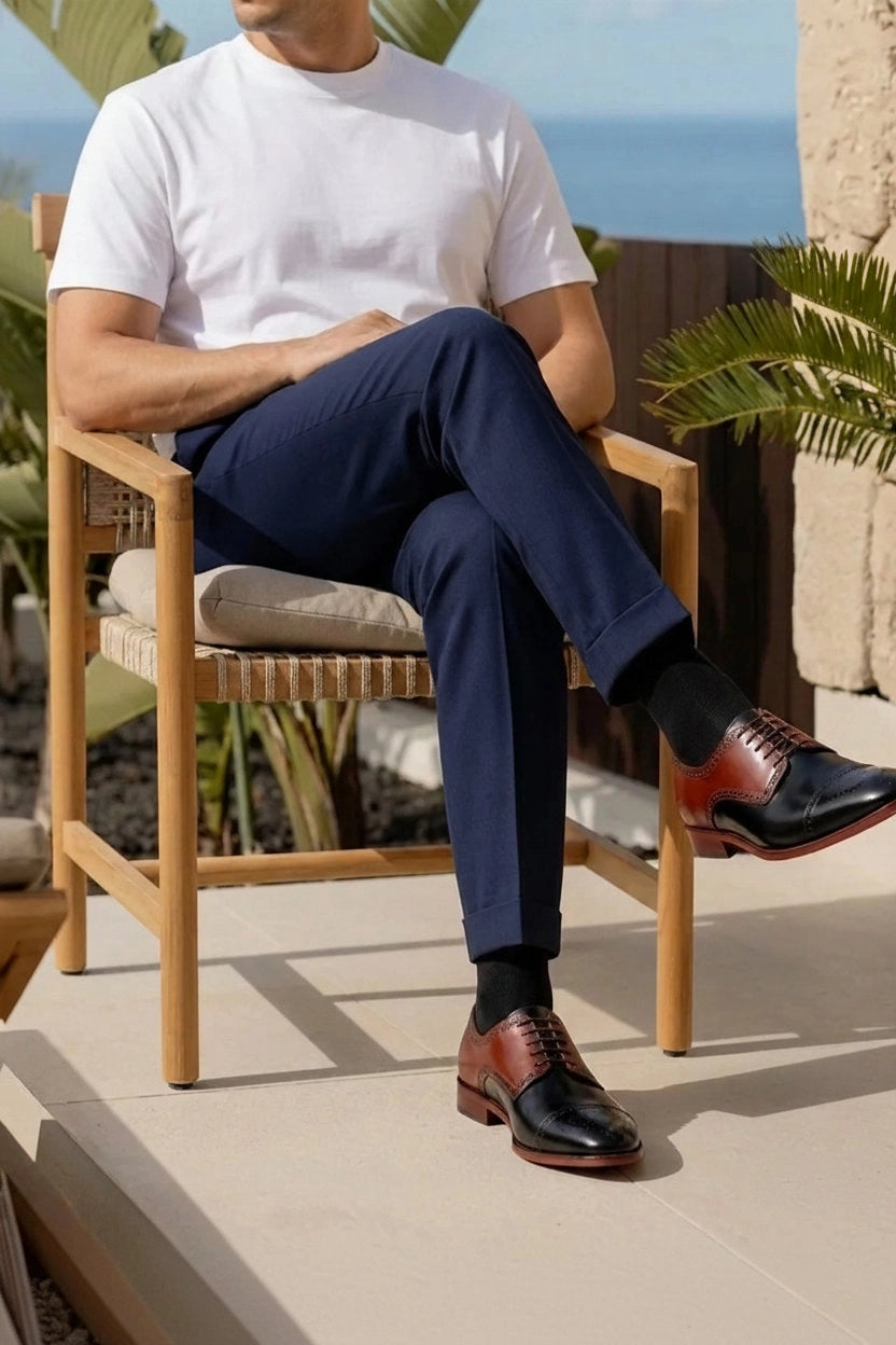 Man wearing cognac and black two-tone Oxford dress shoes with navy trousers at a coastal resort